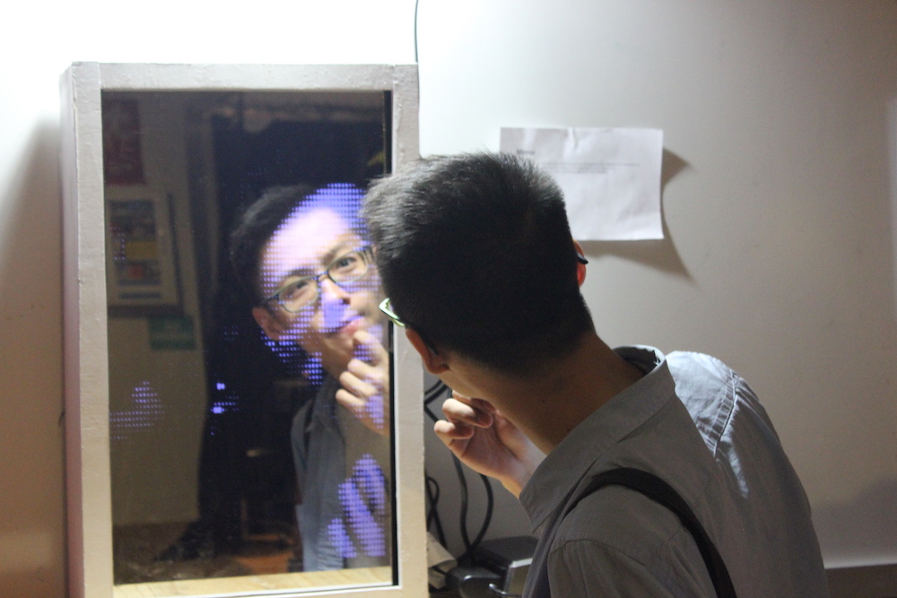 a man looking into a mirror, his face's reflection is pixelated by a screen behind it